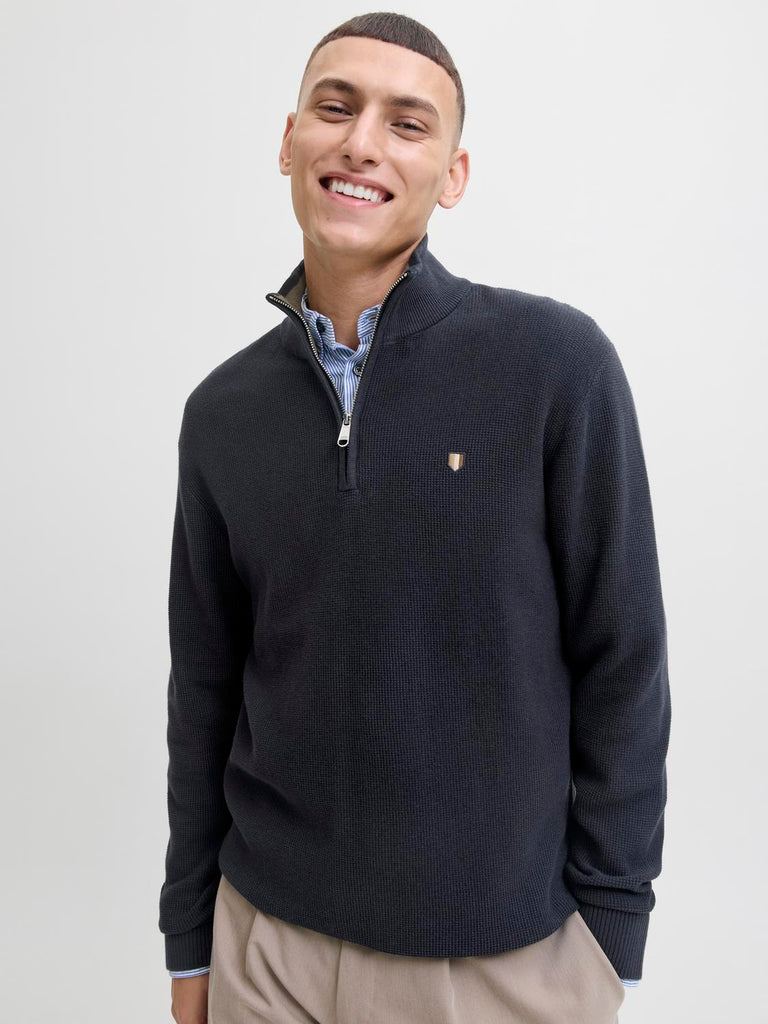 Man wearing a navy blue sweater with a brand logo on a light gray Jack&Jones b