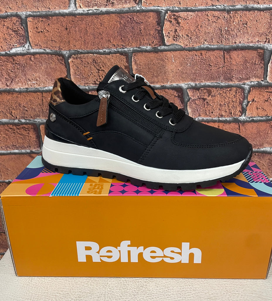 Black sneaker on a colorful box with 'Refresh' branding against a brick wall.
