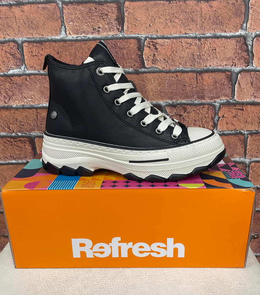 Black and white sneaker on a colorful box with 'Refresh' branding against a brick wall.